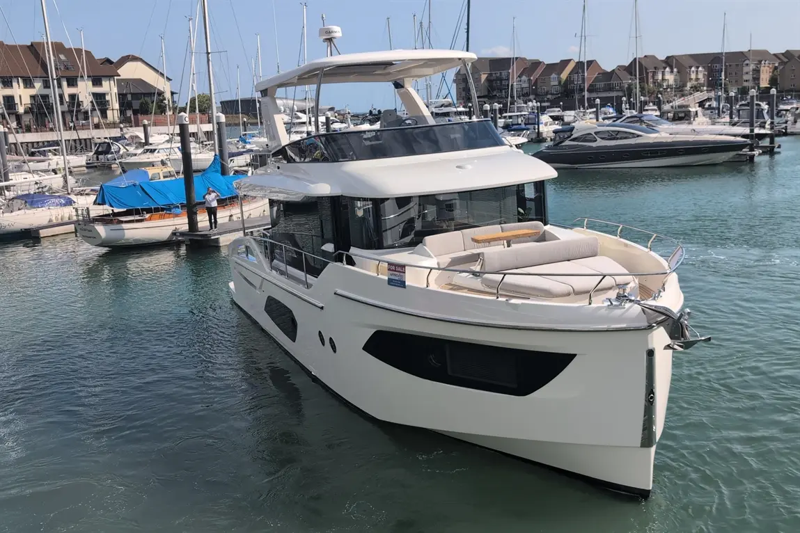 Luxury motorboat docked in the marina, with 'FOR SALE' sign visible, surrounded by various boats and waterfront buildings.